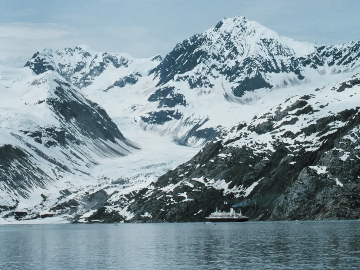 Snow-covered peaks rising above the calm water of Glacier Bay, with a small cruise ship far below