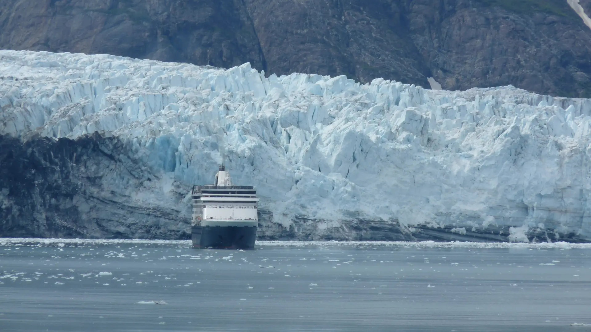 A cruise ship sailing in front of a towering blue-white tidewater glacier in Glacier Bay, Alaska